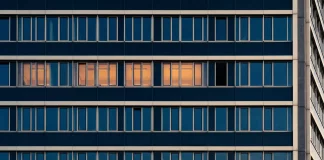 Viertagewoche: Risiko für die deutsche Wirtschaft? Bürogebäudefassade in der Dämmerung, in einer Fensterreihe leuchten vier Fenster warm, das fünfte bleibt dunkel – Sinnbild für die Debatte um die Viertagewoche