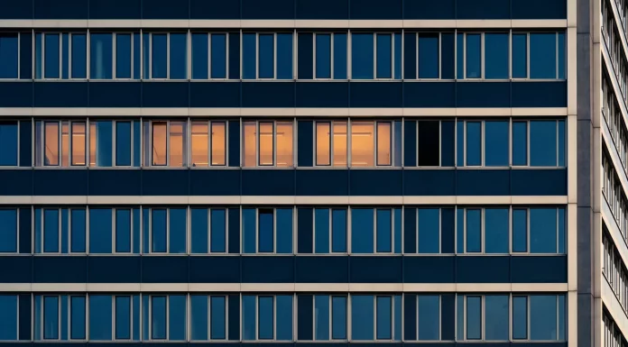 Viertagewoche: Risiko für die deutsche Wirtschaft? Bürogebäudefassade in der Dämmerung, in einer Fensterreihe leuchten vier Fenster warm, das fünfte bleibt dunkel – Sinnbild für die Debatte um die Viertagewoche