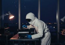 320 Antriebe im Orbit: Warum ENPULSION aus Österreich jetzt selbst zukauft Technikerin im weißen Reinraumanzug prüft ein schwarzes Satelliten-Antriebsmodul an einem Stahltisch, im Hintergrund ein Rollfeld in der blauen Stunde