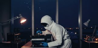 320 Antriebe im Orbit: Warum ENPULSION aus Österreich jetzt selbst zukauft Technikerin im weißen Reinraumanzug prüft ein schwarzes Satelliten-Antriebsmodul an einem Stahltisch, im Hintergrund ein Rollfeld in der blauen Stunde