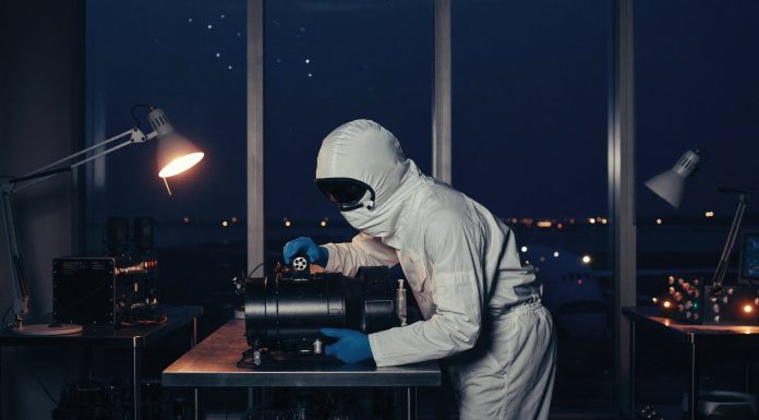 320 Antriebe im Orbit: Warum ENPULSION aus Österreich jetzt selbst zukauft Technikerin im weißen Reinraumanzug prüft ein schwarzes Satelliten-Antriebsmodul an einem Stahltisch, im Hintergrund ein Rollfeld in der blauen Stunde
