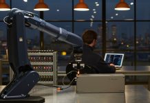 Zwölf Leute, 30 Millionen Dollar: Was Enact aus Zürich den Investoren versprochen hat Navyblauer Roboterarm steckt an einer Werkbank einen Kabelstecker in ein Steuermodul, im Hintergrund ein Ingenieur am Laptop und die Zürcher Skyline zur blauen Stunde